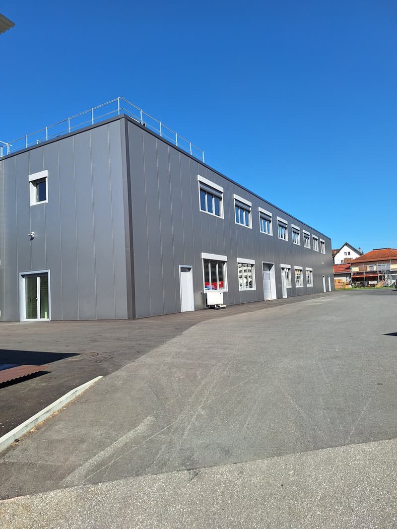 large industrial building, metal cladding, white windows, large entry doors, railing on top, clear surroundings, open parking area