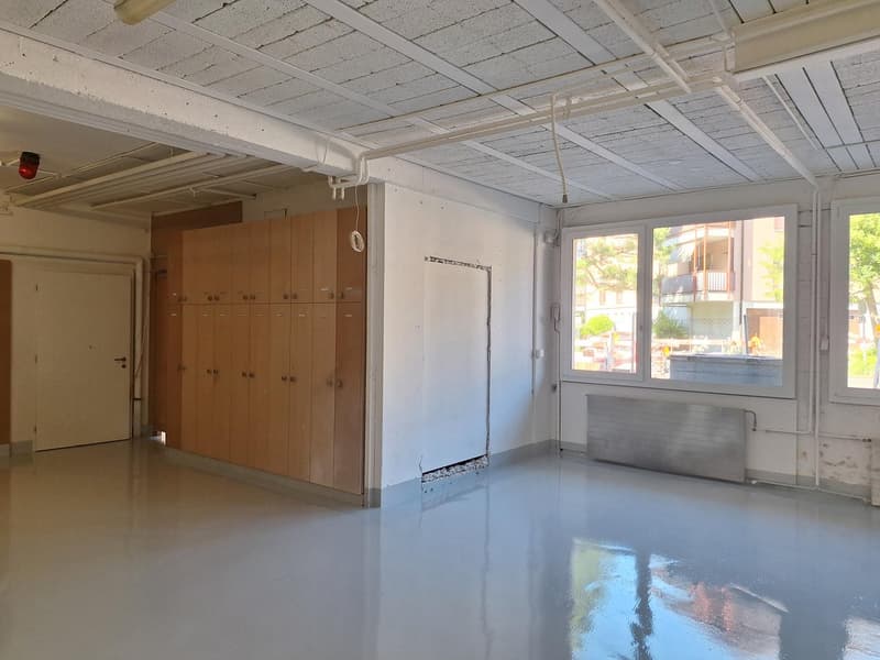 spacious room with white walls, floor, and ceiling, row of wooden lockers, door, two large windows, visible heating panel