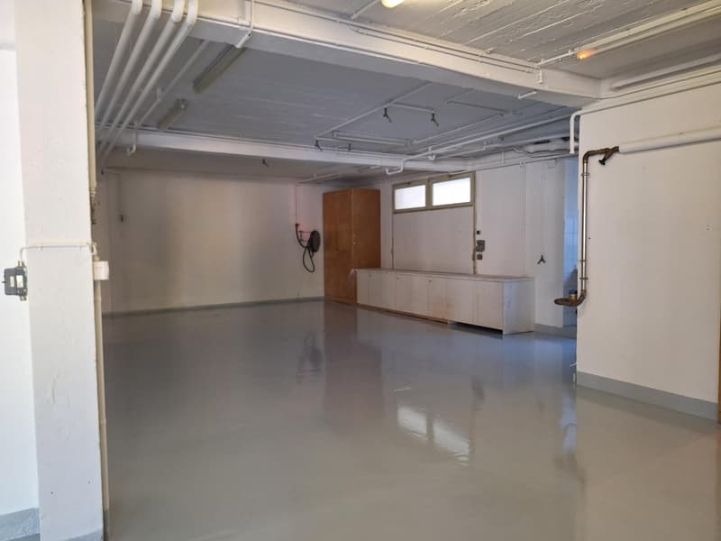 Empty room, smooth concrete floor, ceiling with metal beams, white walls, wooden cabinet, small electrical cabinet