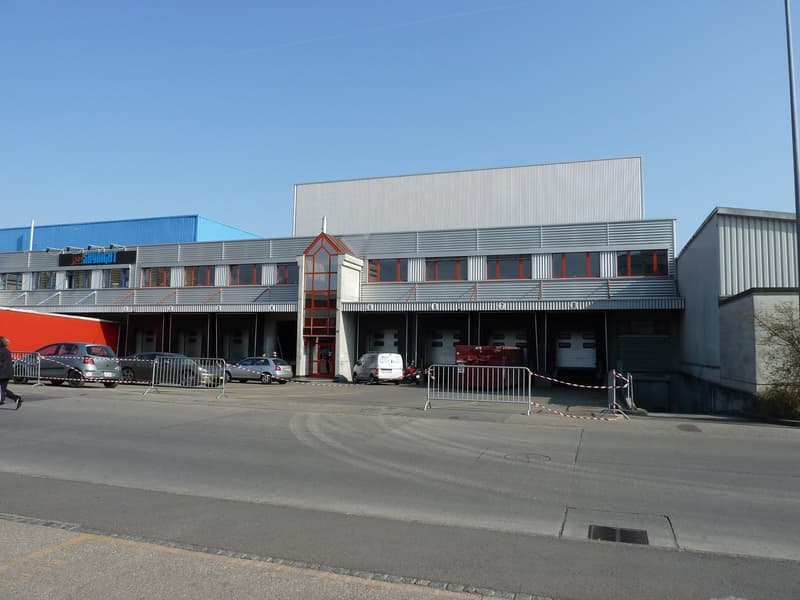 large building with multiple garages, multiple cars parked in front, red dumpster