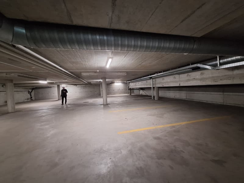 Empty parking lot with concrete floor, yellow markings, and metal beams on the ceiling.