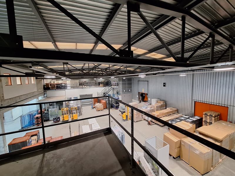 large warehouse with metal beams, glass railings, forklifts, stacked boxes, metal shelves