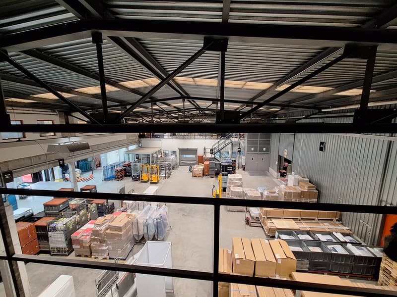 large warehouse with high ceilings, metal beams, multiple pallets, forklifts, and storage boxes