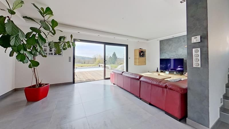 Spacious living room with large sliding glass doors leading to a balcony or terrace, hardwood floors, red sofa, wall-mounted TV, and a potted plant.