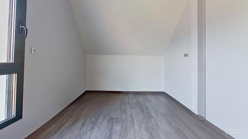 Empty room with white walls and a hardwood floor. The room has a window and appears to be a bedroom or living space.