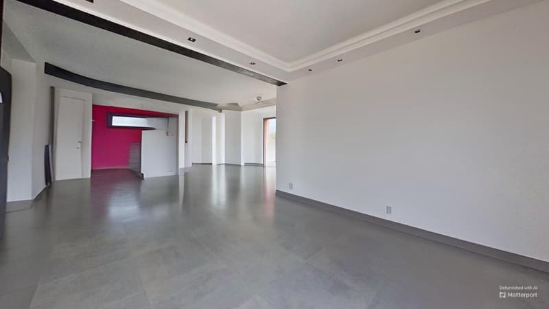 Large open-plan living space with high ceilings, white walls, and gray tile flooring. The room has a modern, minimalist design with recessed lighting and a red accent wall visible in the background.