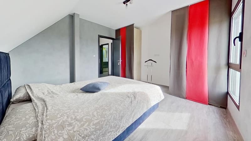 Spacious bedroom with gray walls, large windows, patterned bedding, built-in closet, and red curtains.