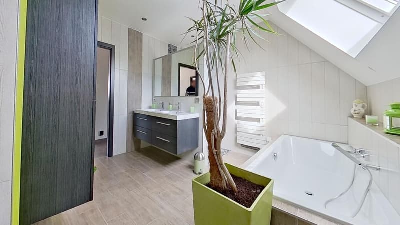 Spacious bathroom with modern vanity, large bathtub, and a potted plant adding a natural touch. The room features a raised floor and a fireplace, creating a luxurious and relaxing atmosphere.