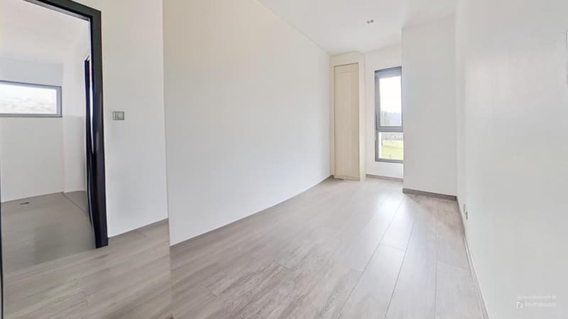 Spacious room with white walls, light-colored hardwood flooring, and large windows providing natural light. The room appears to be empty, ready for furnishing and decorating.