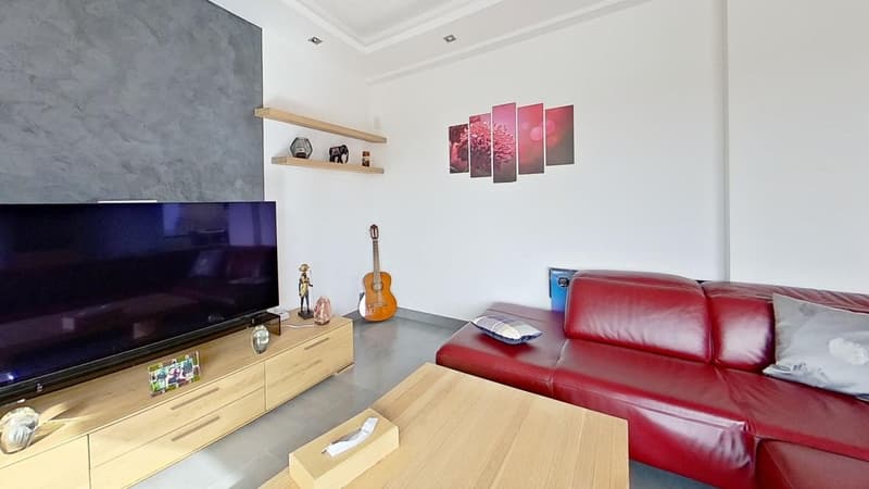 Spacious living room with white walls, large TV, wooden entertainment unit, red leather sofa, guitar, and decorative shelves with figurines and artwork