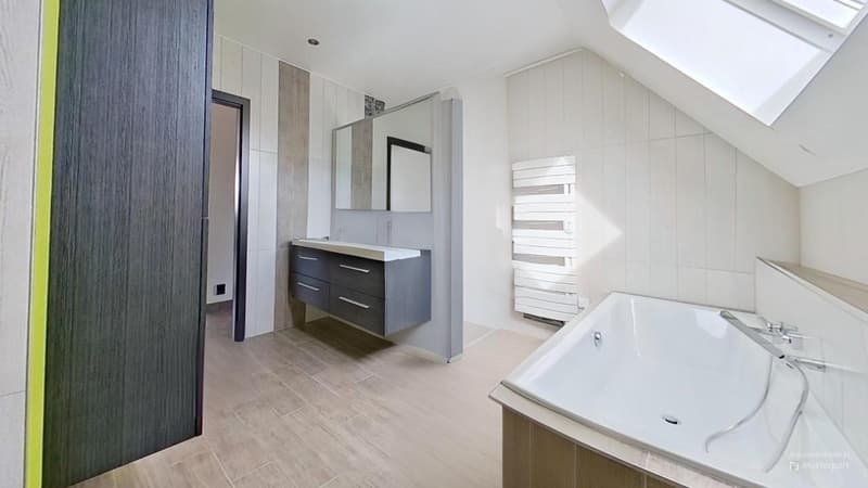 Spacious bathroom with white walls, wood-like tile flooring, a vanity with drawers, a large mirror, and a bathtub.