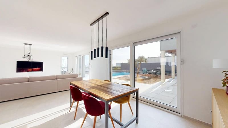 modern room with wooden dining table, glass sliding doors, open space to garden with pool, chandeliers