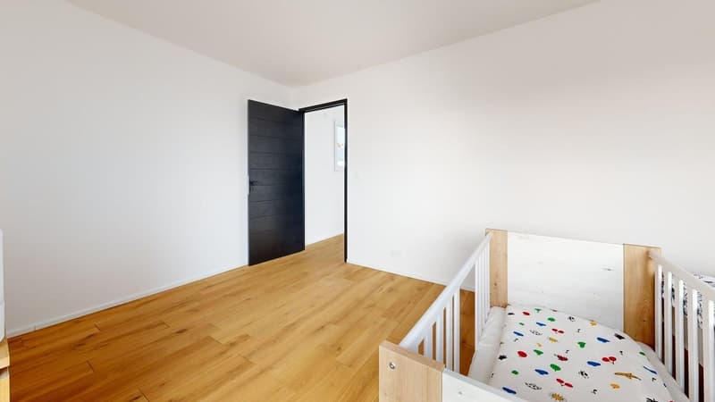 Empty room with white walls, hardwood floor, black door, open door, small crib
