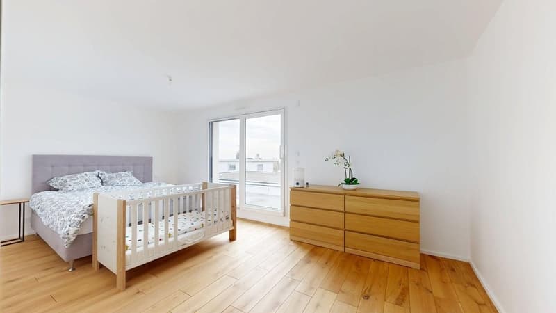 White walls, wooden floor, a bed, a crib, a side table, a cabinet, and a flower vase.