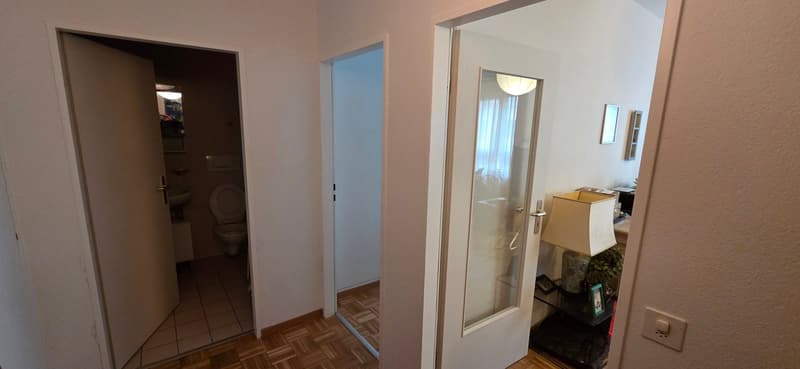 Corridor leading to bathroom and hallway with light fixtures, wooden floor, and picture frames on wall