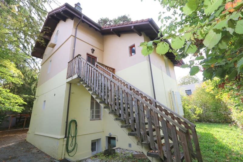 two-story house, yellow paint, wooden staircase, balcony, wooden railings, small garden, green hose