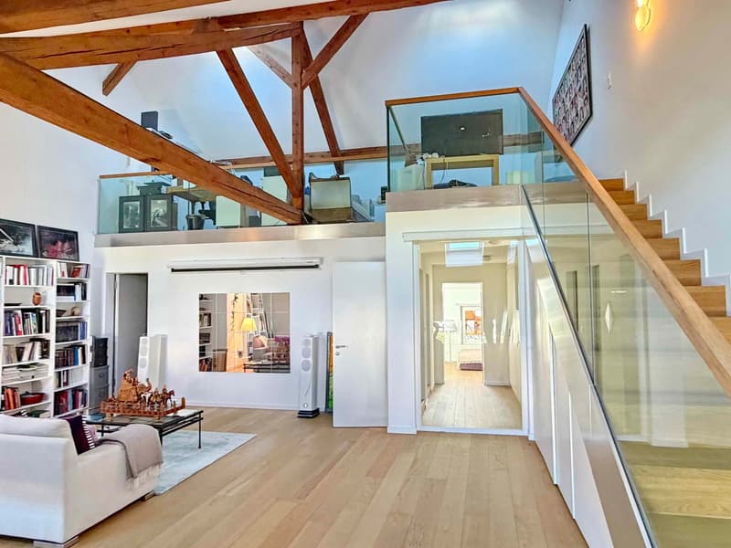 Open-plan living area, wooden flooring, high ceiling, stairs to upper level, glass railing, balcony on the upper level, glass balcony railing, mirror on wall, books, speakers