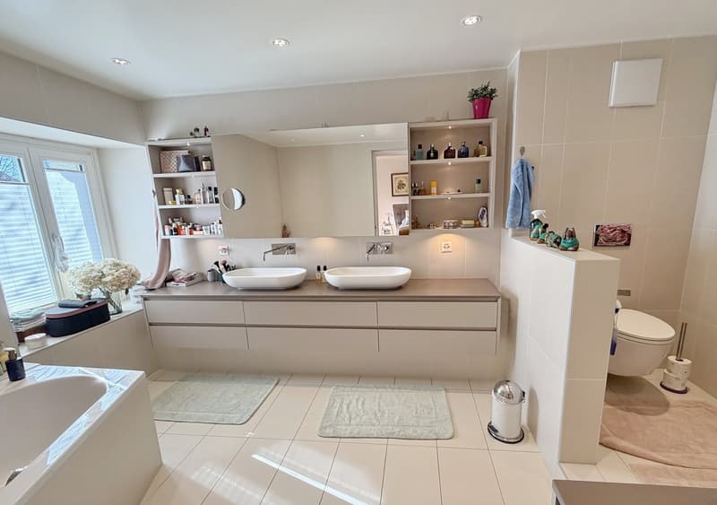 modern bathroom with white tiles, large mirror, two basins, bathtub, and a toilet