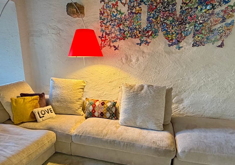 a L-shaped beige couch, a few cushions, a colorful butterfly art above the couch, a red lamp