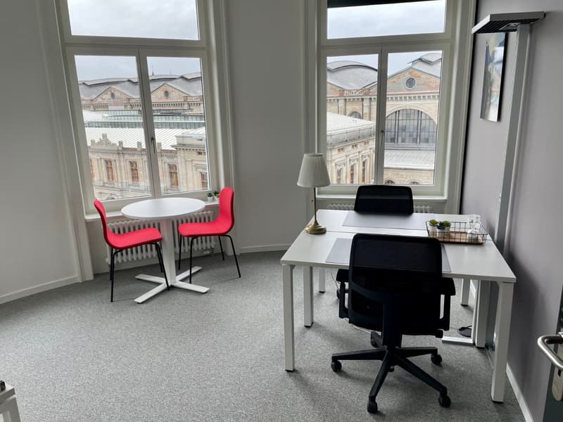 Office room, round white table with red chairs, white desks with black chairs, lamps, radiators, gray carpeting