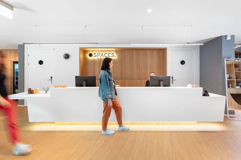 Reception desk, wooden paneling, monitor, staff member, wooden flooring, open space, ceiling lights