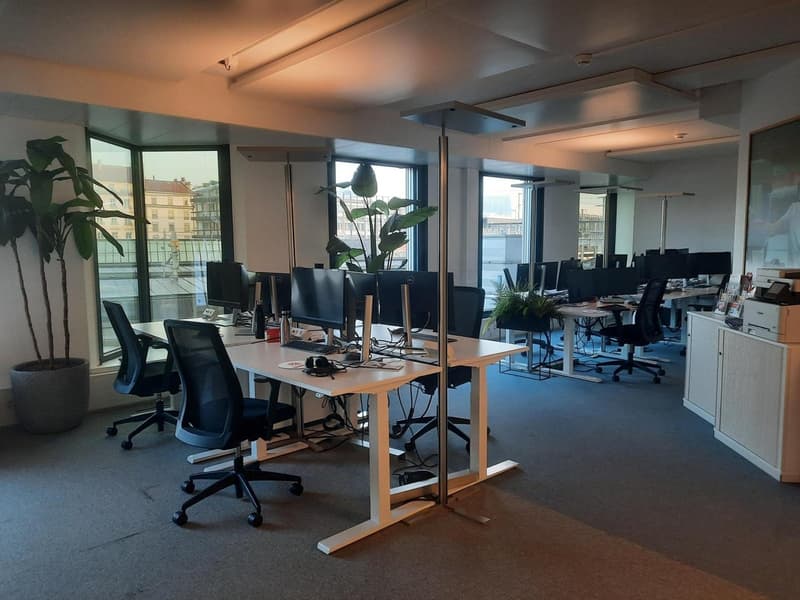 open space with desks, chairs, multiple computers, windows with city view