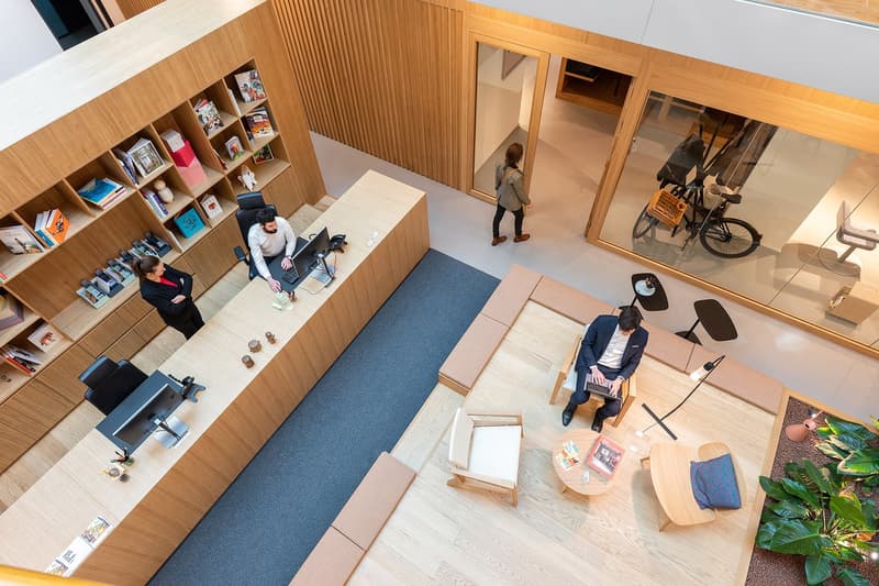 ample space, wooden interior, desks, bookshelves, blue carpet, lamps, a person walking