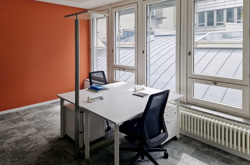 Modern office space with large windows, white desk, black office chair, and orange accent wall