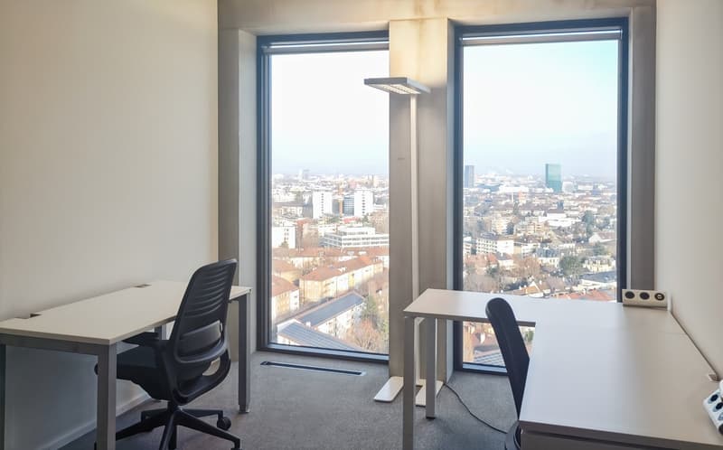 Spacious office with large windows offering a panoramic view of the city skyline. The room features a desk, chairs, and other office equipment. The overall design is modern and minimalist, creating a professional and functional workspace.