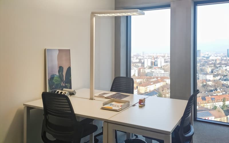 Spacious office with large windows offering a panoramic view of the city skyline. The office features a modern desk, a desk lamp, and a framed artwork on the wall. The room has a clean and minimalist design with neutral colors.