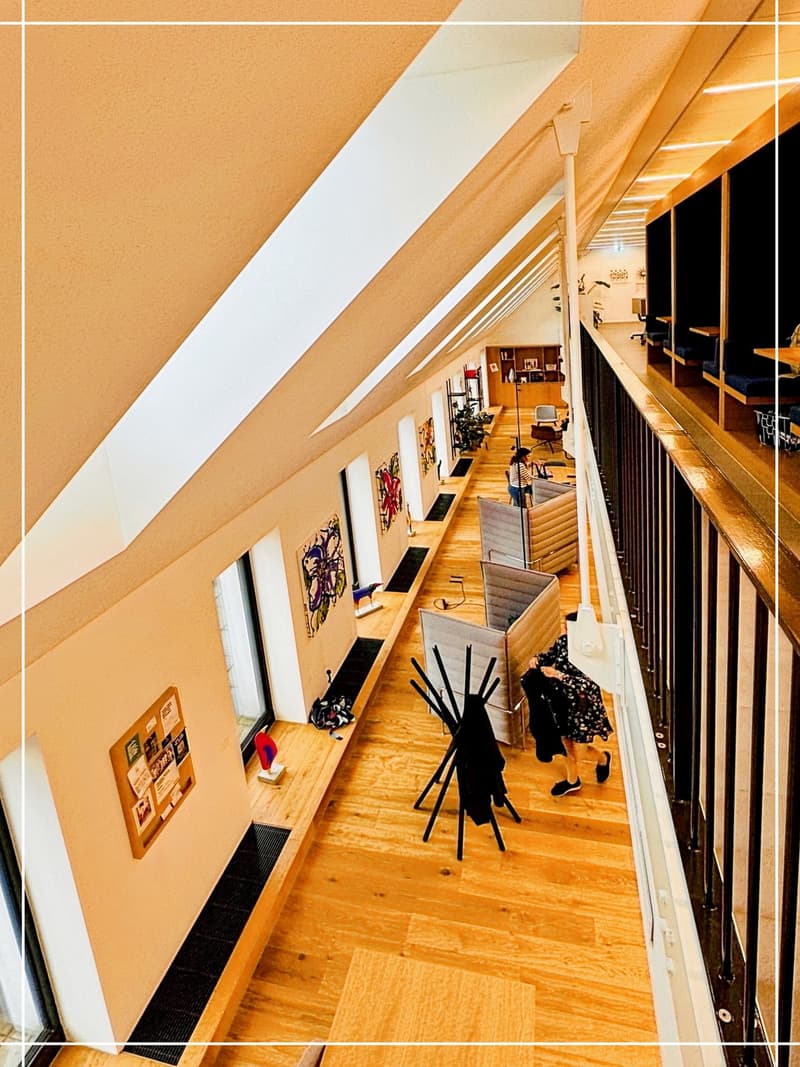 wooden floor, wooden benches, black railings, paintings on the wall, people sitting