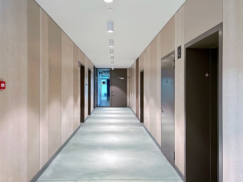 A hallway in a building with several doors, recessed lighting, and beige walls.
