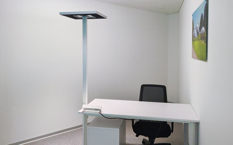 Modern office with white walls, desk, black office chair, standing lamp, storage cabinet, painting on the wall.