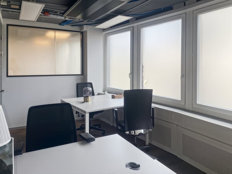 modern office room with white walls, large windows, white desks, black chairs, lamp, basket, and ceiling lights