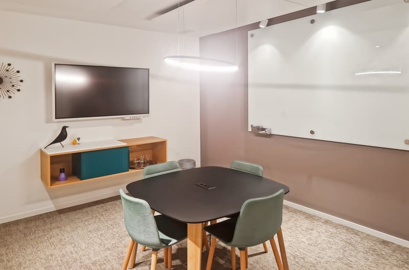 a conference room with a round table, four chairs, a shelf with decor and a TV, and a board