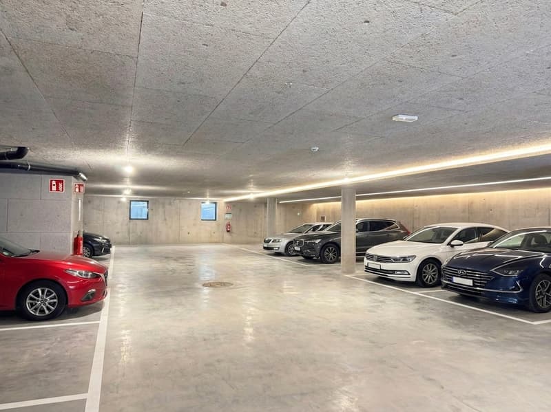 underground parking lot with multiple cars parked, fire extinguisher, fire alarm, surveillance camera, pillars, white floor lines, lighting