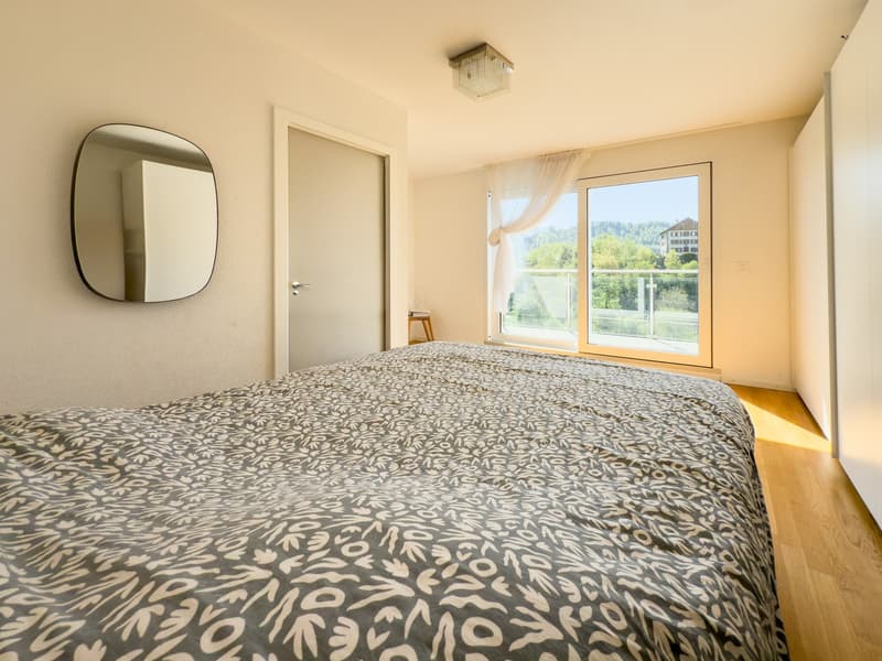 Spacious bedroom with large window overlooking a scenic outdoor view, hardwood floor, patterned bedspread, and a wall mirror.