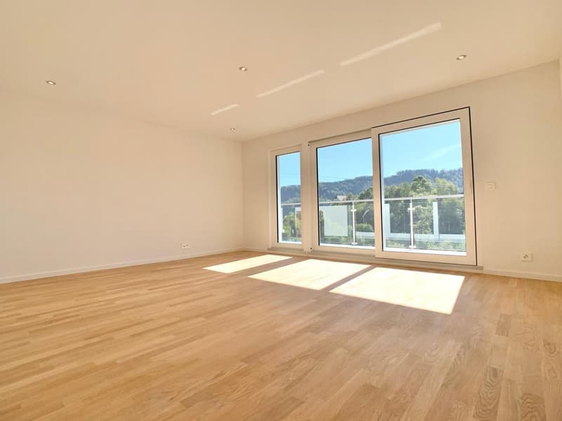 Spacious living room with large windows offering a scenic view, hardwood flooring, and an abundance of natural light.