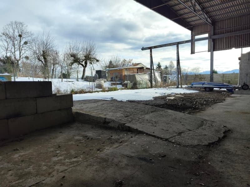 Exposed building exterior, large concrete block, concrete floor, snow-covered field, metal poles, tractor, mountains in the distance