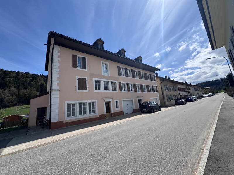 3 story building, beige and white exterior, multiple windows, garage, cars parked in front