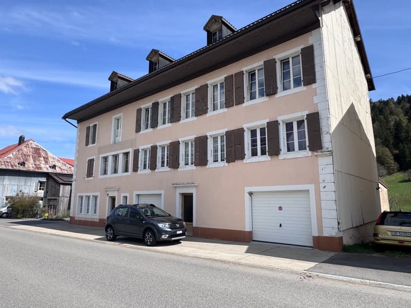 3 story building, beige and brown exterior, multiple windows, 2 garages, cars parked in front