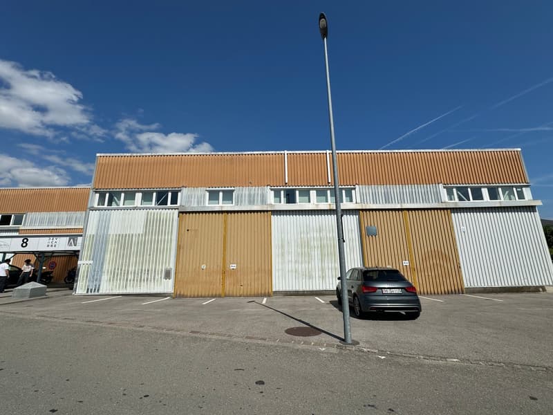 Industrial building with large double doors, several windows, car parked in front