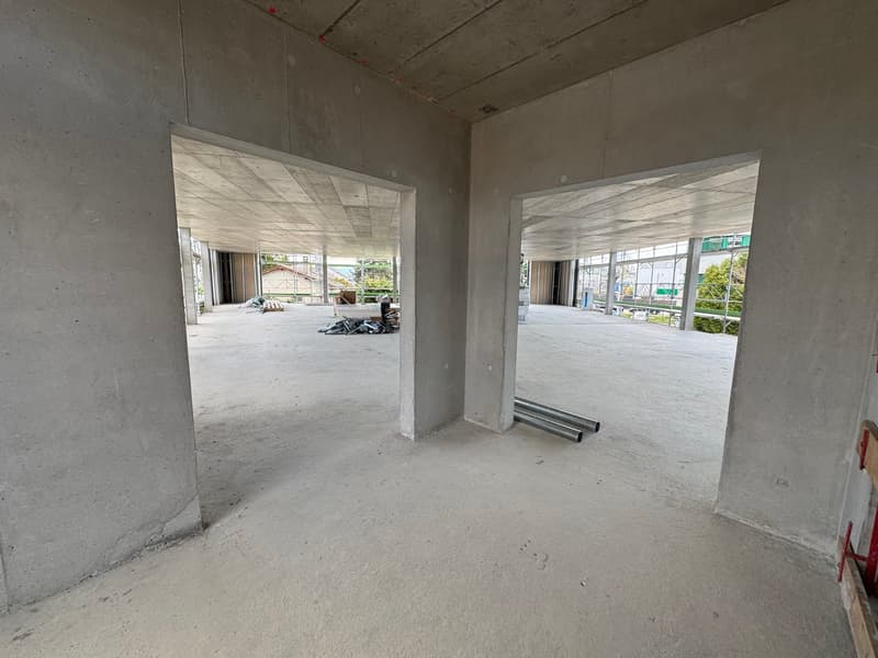 Empty room with concrete walls and floor, two open doorways, construction materials scattered on the floor