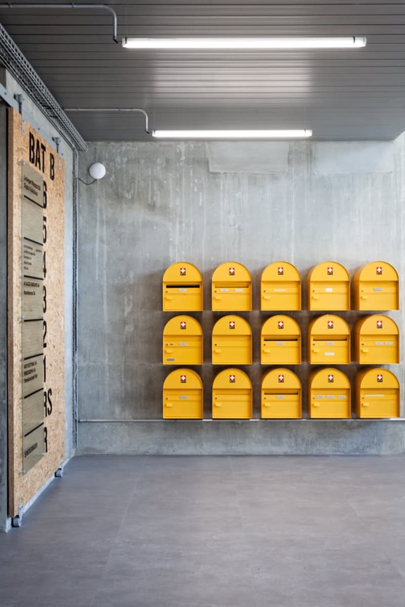 The image shows a storage facility with rows of yellow lockers or mailboxes on the wall. The room has a concrete floor and gray walls with fluorescent lighting fixtures overhead.