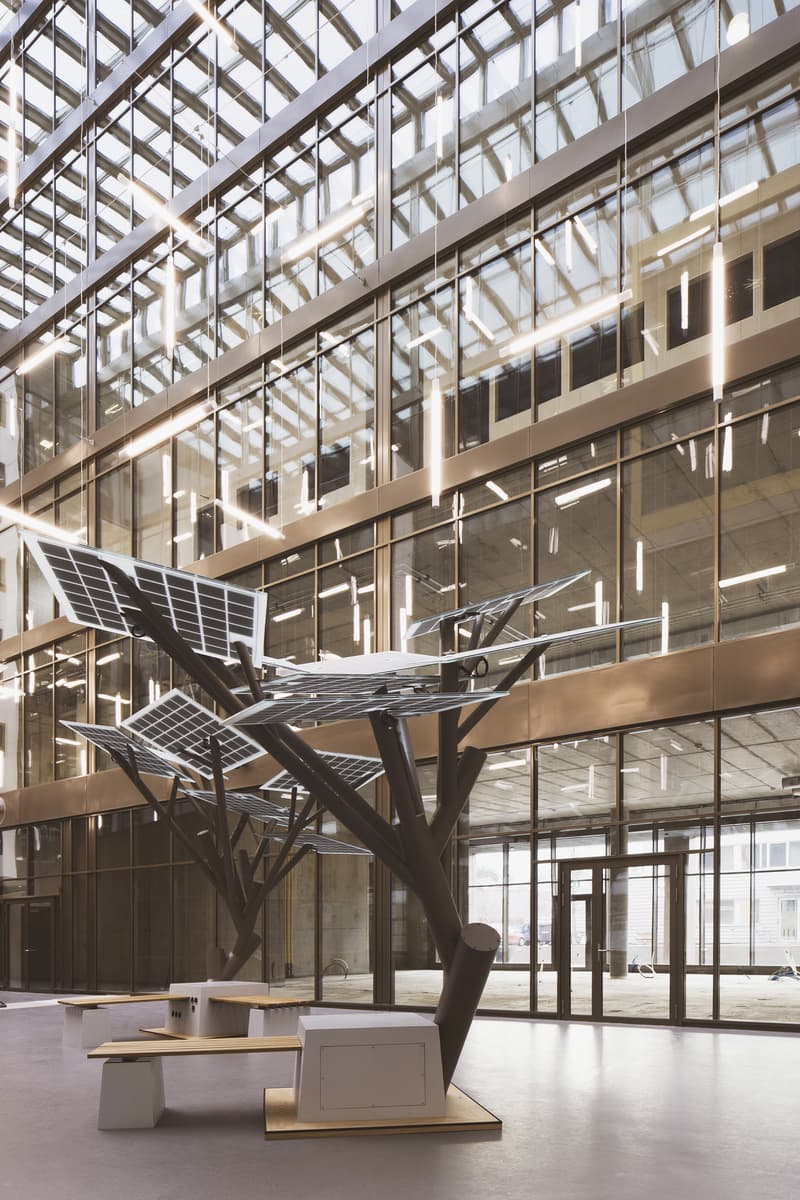 Large open space with glass walls and ceiling, modern architectural design, sculptural metal structure with solar panels, seating areas with benches