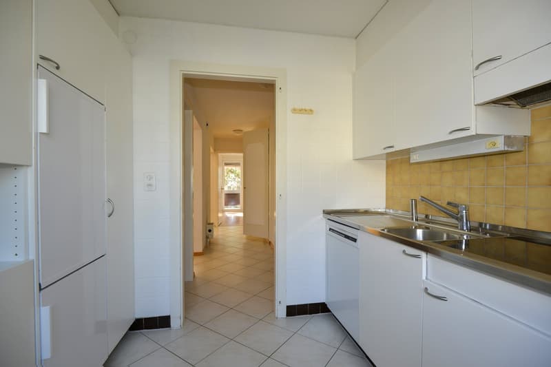 modern kitchen with tiled floor and white walls, double sink with faucet, dishwasher, refrigerator, cabinets, tiled hallway