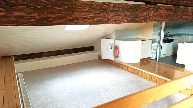 The image shows an attic or loft space with a raised floor. The space has wooden beams and walls, and appears to be used for storage or additional living space. There are some appliances and boxes visible, suggesting it may be used as a utility or storage