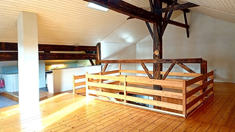 Spacious attic with wooden beams, wooden floors, and bunk beds. The space appears to be a loft or attic conversion, with a balcony or terrace visible.