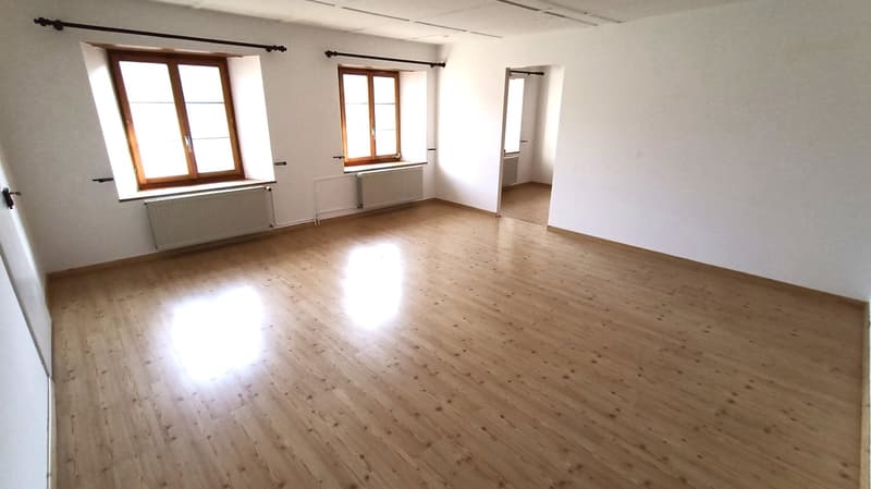Large open room with hardwood floors, white walls, and several windows providing natural light. The room appears to be empty, ready for furnishing and use.
