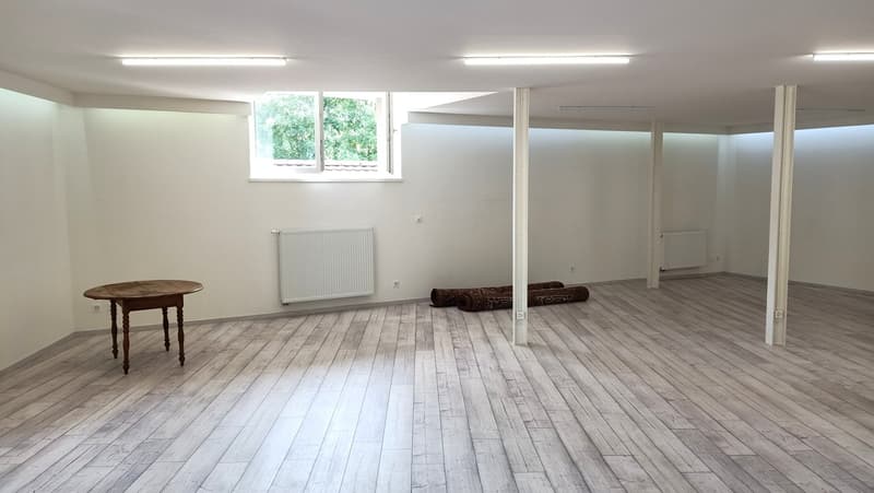 Empty room with white walls, wooden floor, table, window, and radiators.